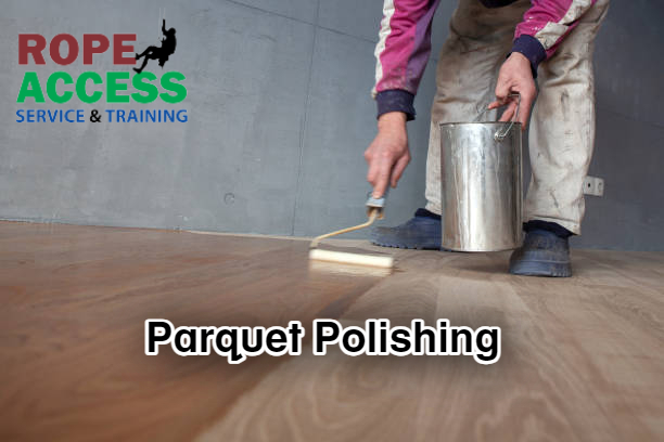 Professional from parquet polishing service in Kathmandu is polishing wooden parquet. He is holding a bucket of polishing liquid and polishing through roller brush.